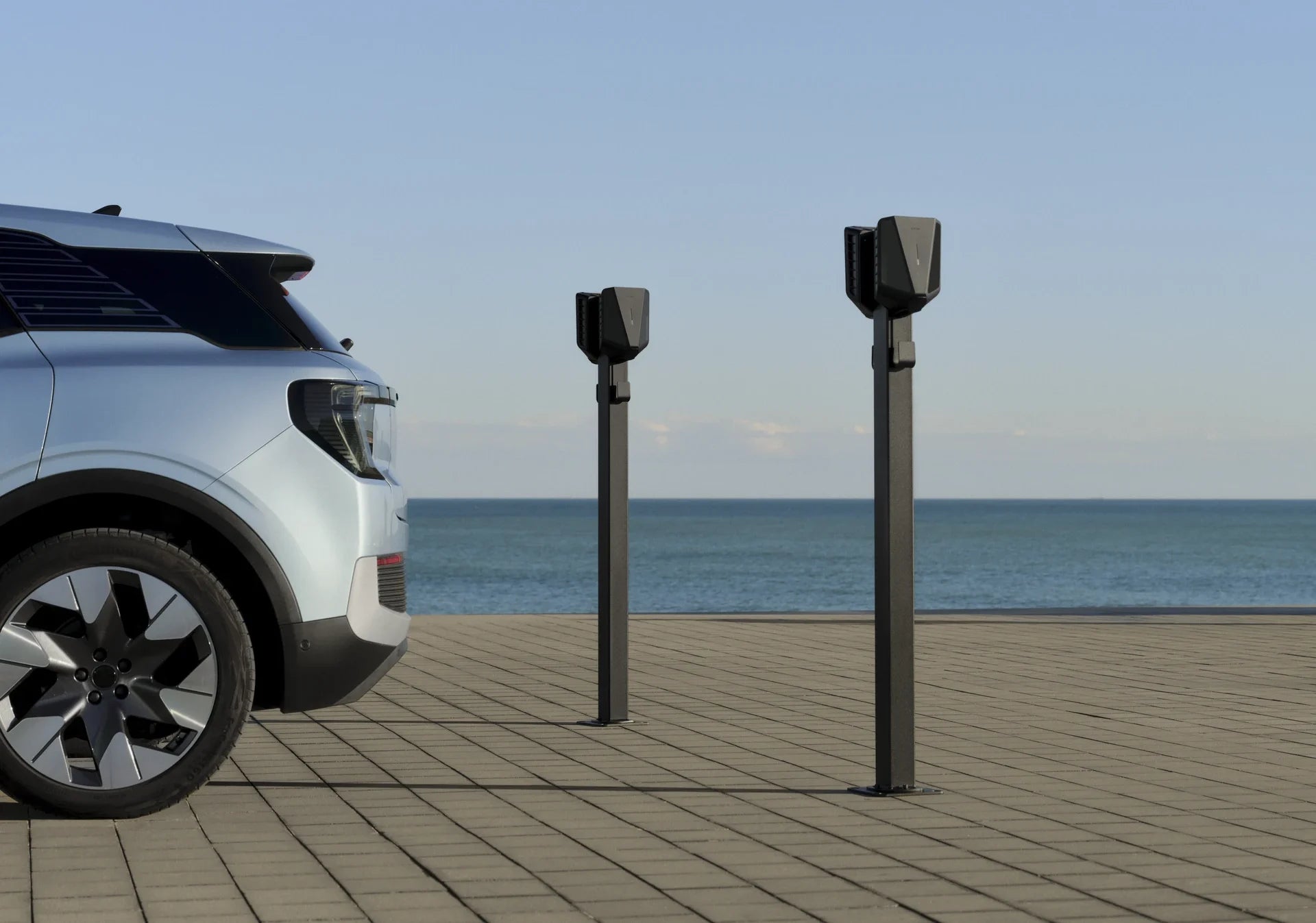 Zwei Ladestationen auf Standfüßen neben einem Elektroauto